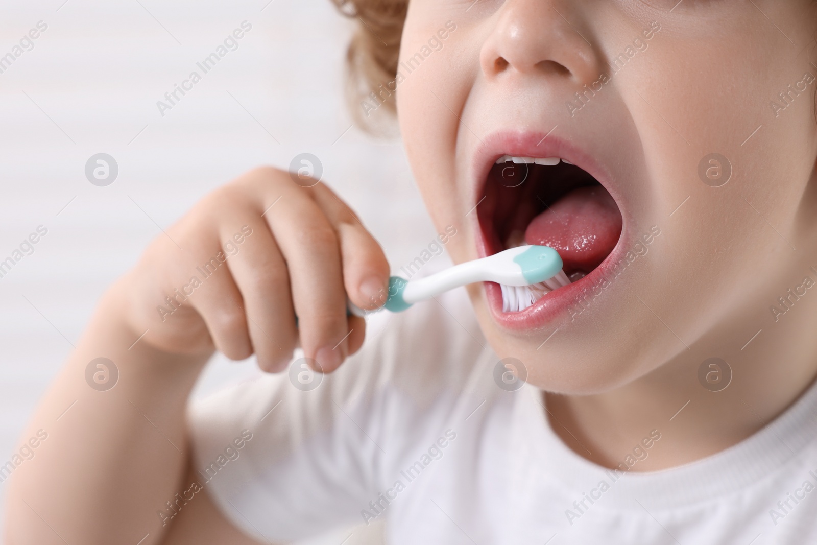 Photo of Little boy brushing his teeth with plastic toothbrush on white background, closeup