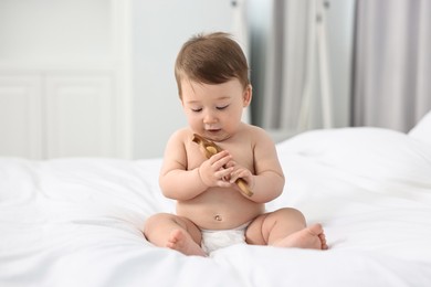 Cute baby boy with wooden rattle on bed at home