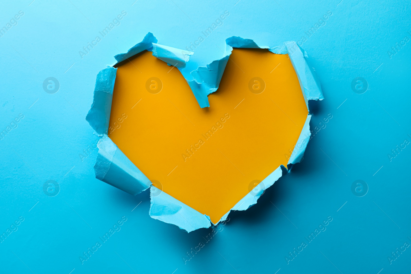 Photo of Torn heart shaped hole in light blue paper on yellow background