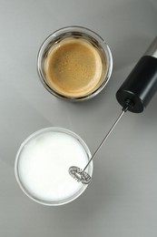 Mini mixer (milk frother), whipped milk and coffee in glasses on grey background, flat lay