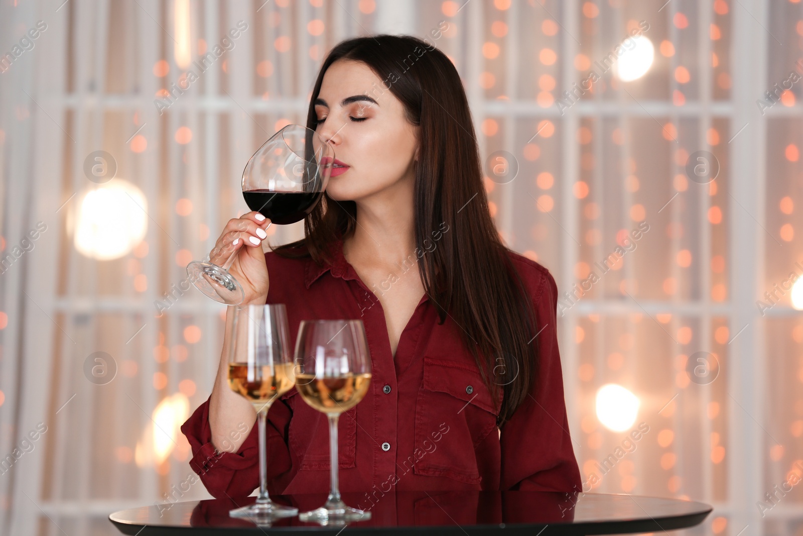 Photo of Beautiful young woman tasting luxury wine at table indoors