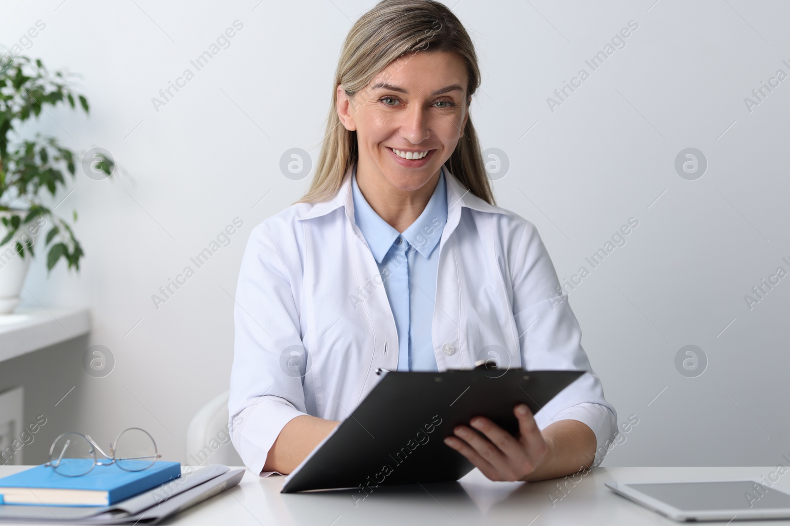 Photo of Portrait of happy doctor with clipboard at white table in hospital