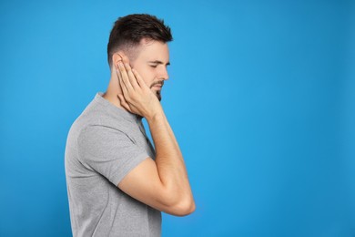 Photo of Young man suffering from ear pain on light blue background. Space for text