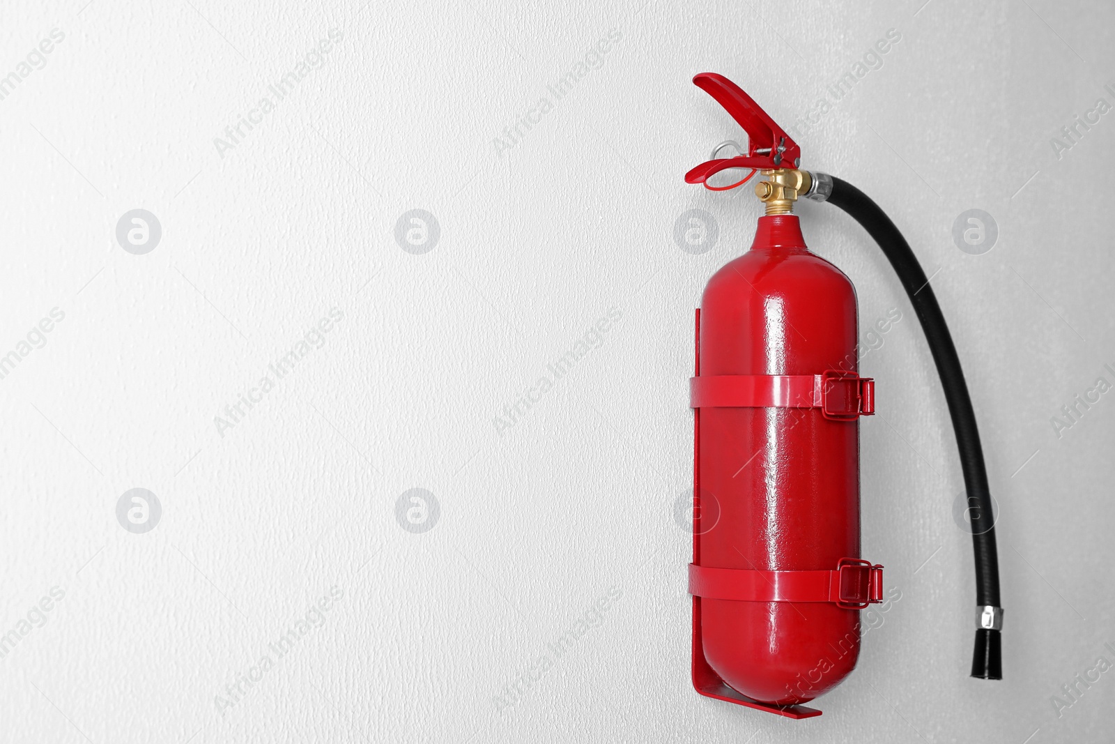 Photo of Fire extinguisher hanging on white wall. Space for text