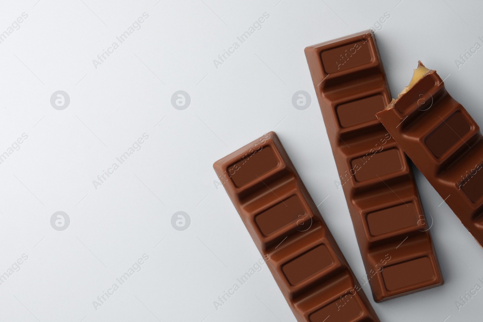 Photo of Delicious chocolate bars on light blue background, flat lay. Space for text