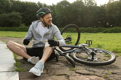 Photo of Man applying bandage onto his knee near bicycle outdoors