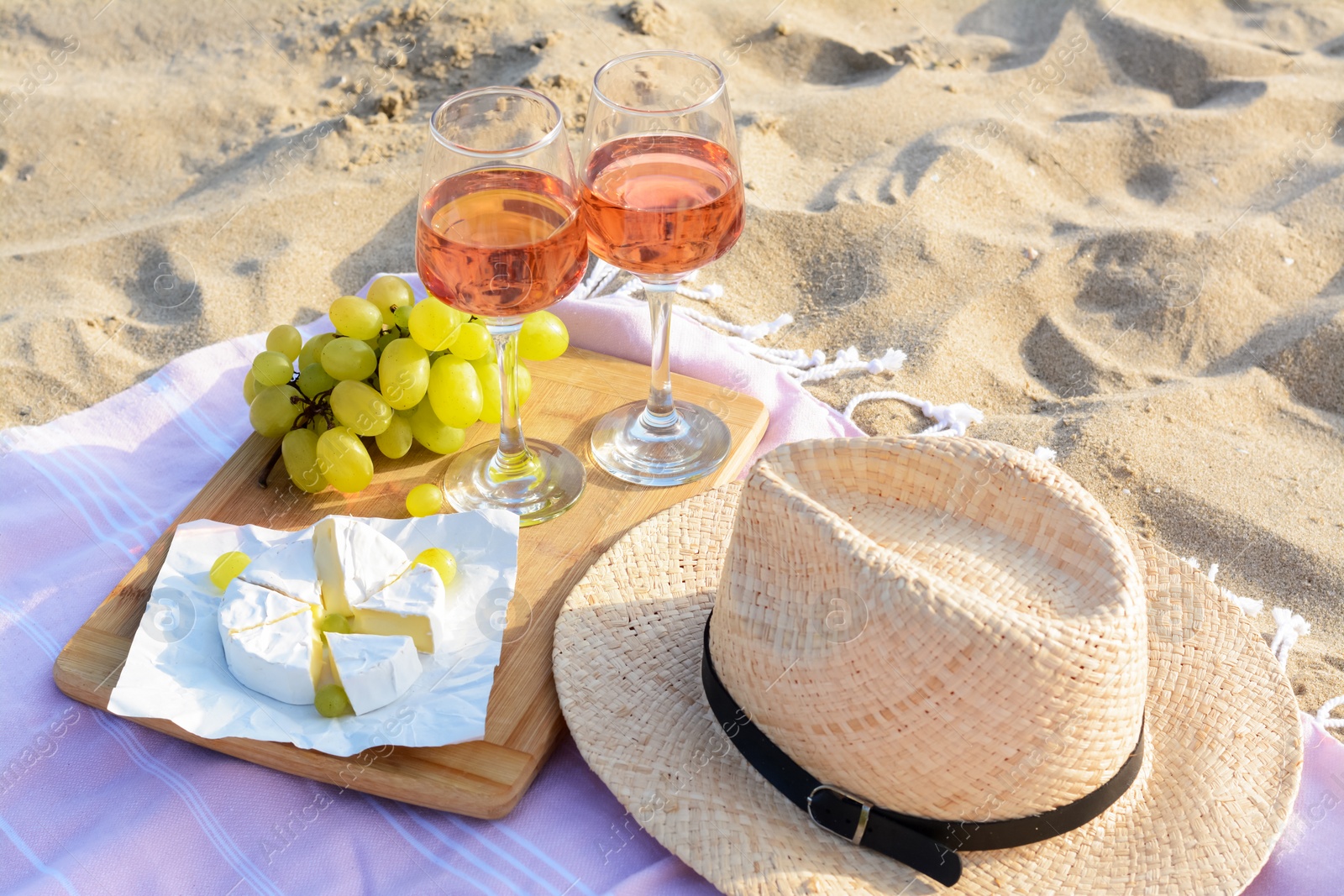 Photo of Glasses with rose wine and snacks for beach picnic on sand outdoors