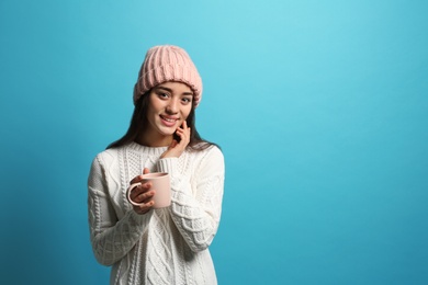 Photo of Young woman in sweater with cup of hot coffee on color background, space for text. Winter season