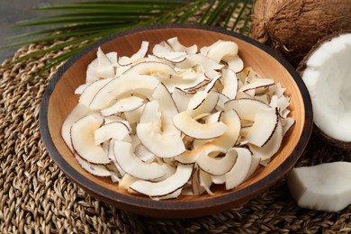 Photo of Tasty coconut chips in bowl on wicker mat