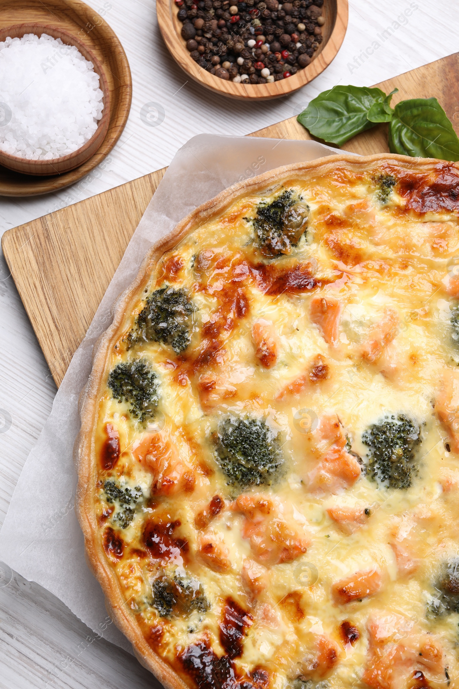 Photo of Delicious homemade quiche with salmon, broccoli, basil leaves and spices on white table, flat lay
