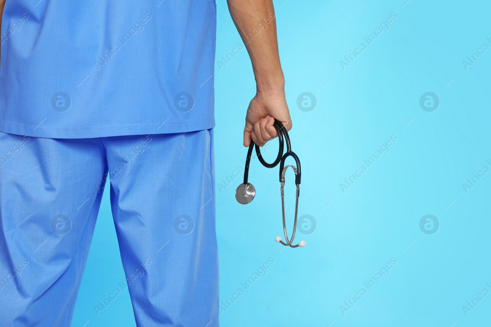 Photo of Male doctor holding stethoscope on color background, closeup with space for text. Medical object