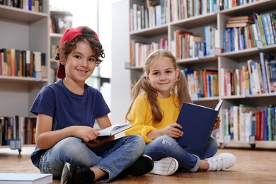 Cute little children reading books on floor in library