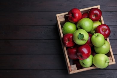 Photo of Fresh ripe red and green apples in wooden crate on black table, top view. Space for text