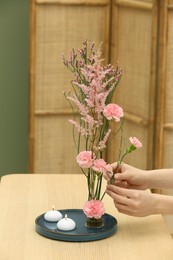 Photo of Woman creating stylish ikebana with beautiful pink flowers at table, closeup
