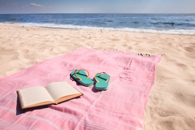 Photo of Pink striped beach towel, flip flops and book on sandy seashore