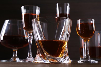 Photo of Different delicious liqueurs in glasses on wooden table, closeup