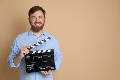 Making movie. Smiling man with clapperboard on beige background. Space for text