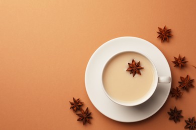 Cup of tea with milk and anise stars on brown background, flat lay. Space for text