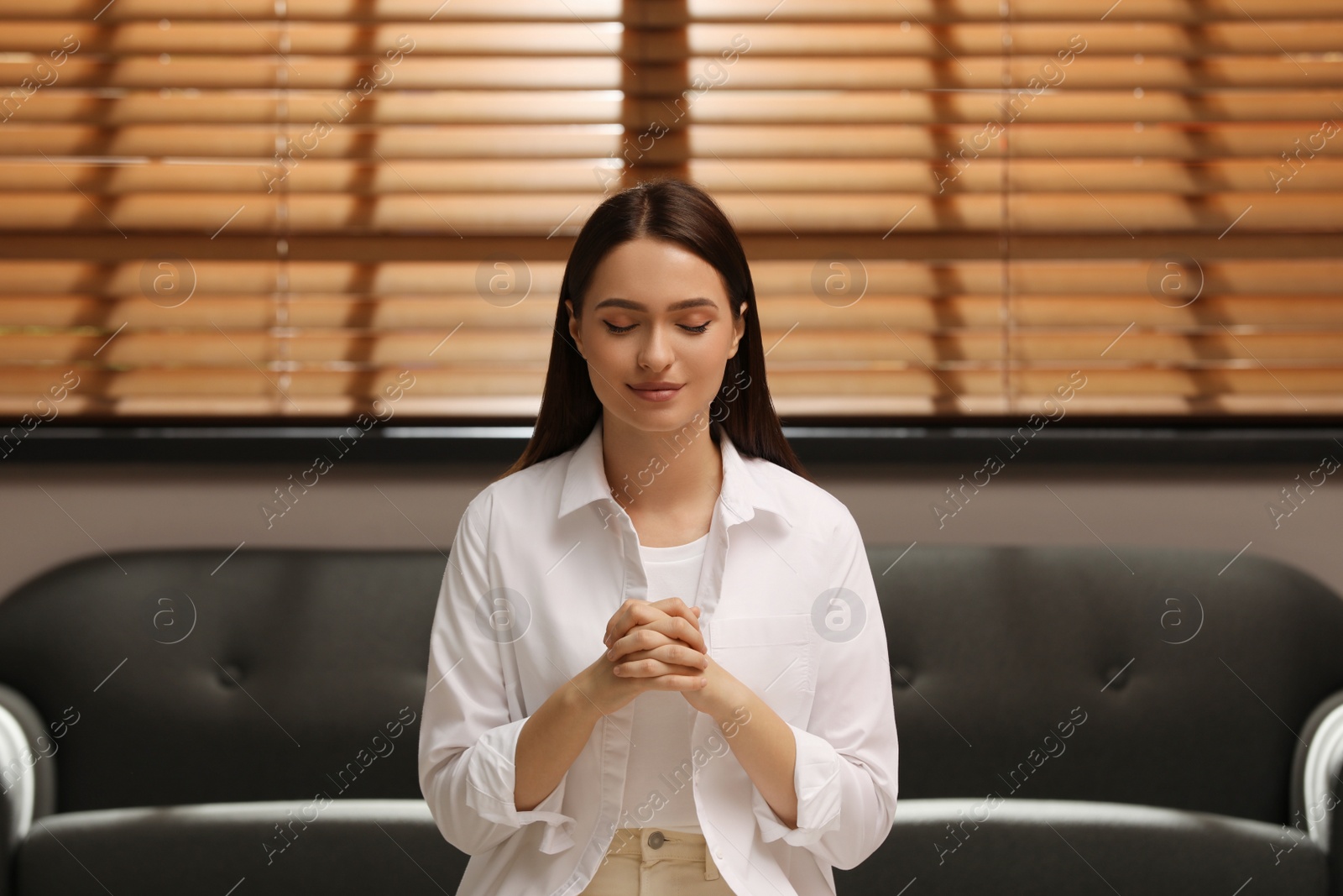 Photo of Religious young woman with clasped hands praying indoors