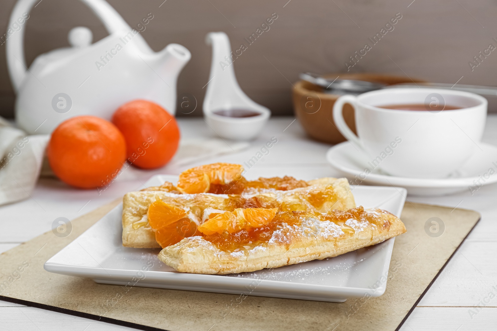 Photo of Fresh tasty puff pastry with sugar powder and tangerines on white wooden table, closeup