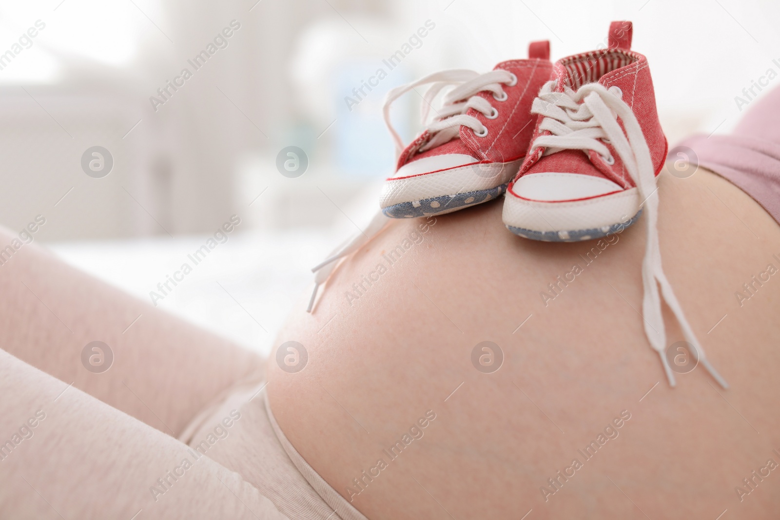 Photo of Pregnant woman with baby booties on blurred background, closeup view