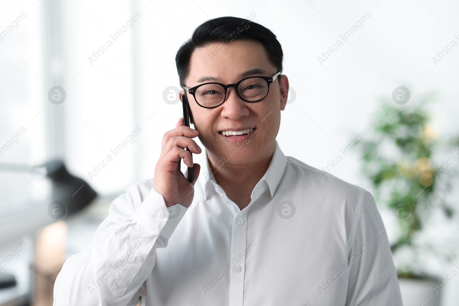 Photo of Portrait of smiling businessman talking by smartphone in office