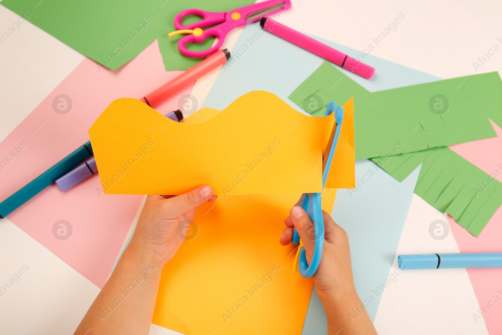Photo of Little girl cutting color paper with scissors at table, above view