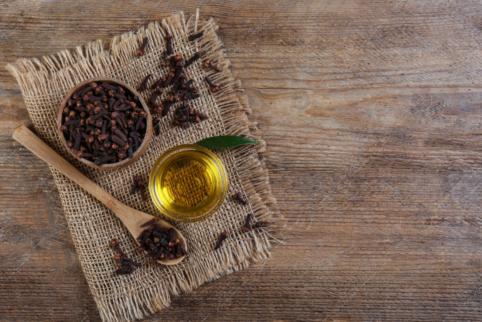 Photo of Essential oil and dried cloves on wooden table, flat lay. Space for text