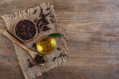 Essential oil and dried cloves on wooden table, flat lay. Space for text