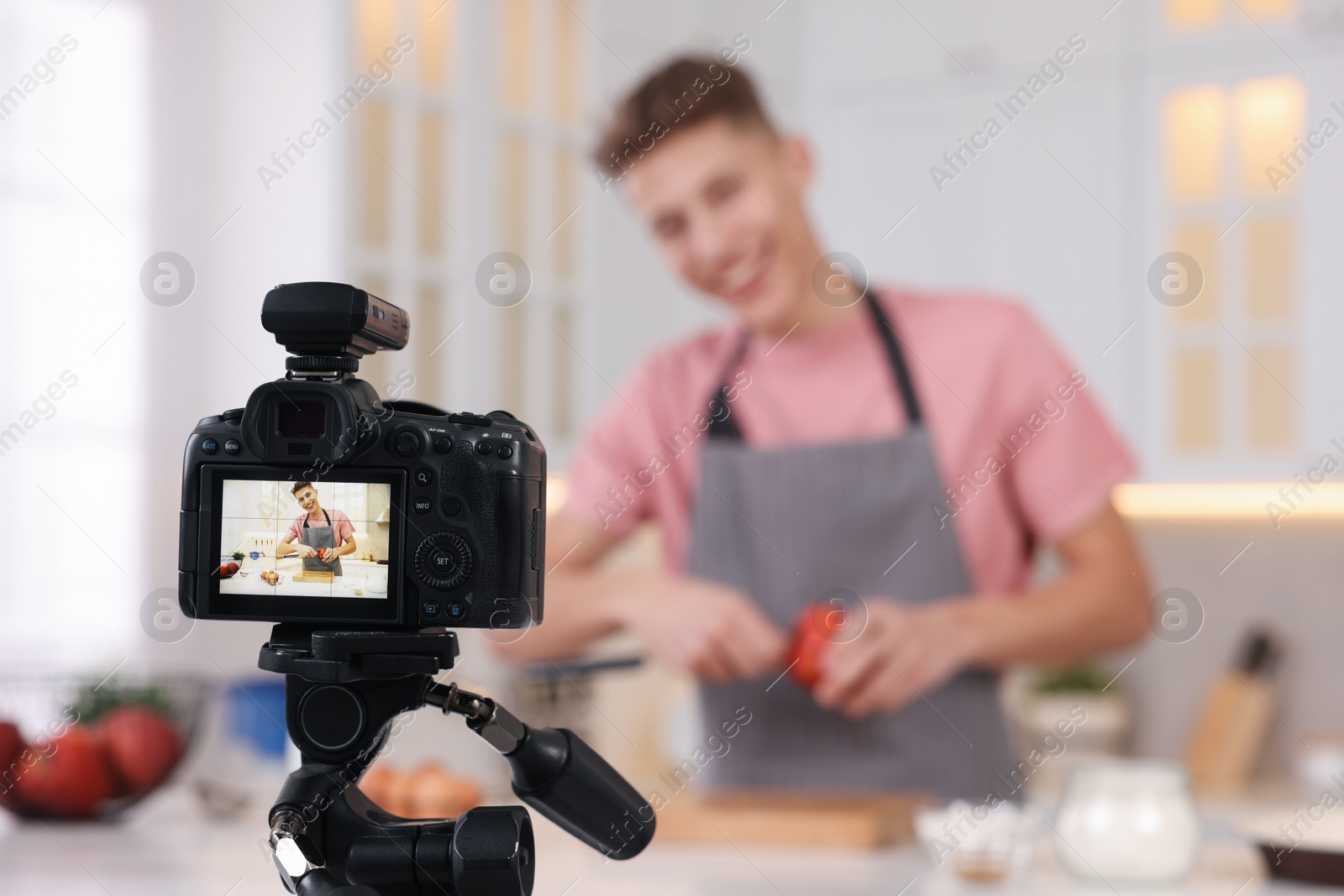 Photo of Food blogger cooking while recording video in kitchen, focus on camera