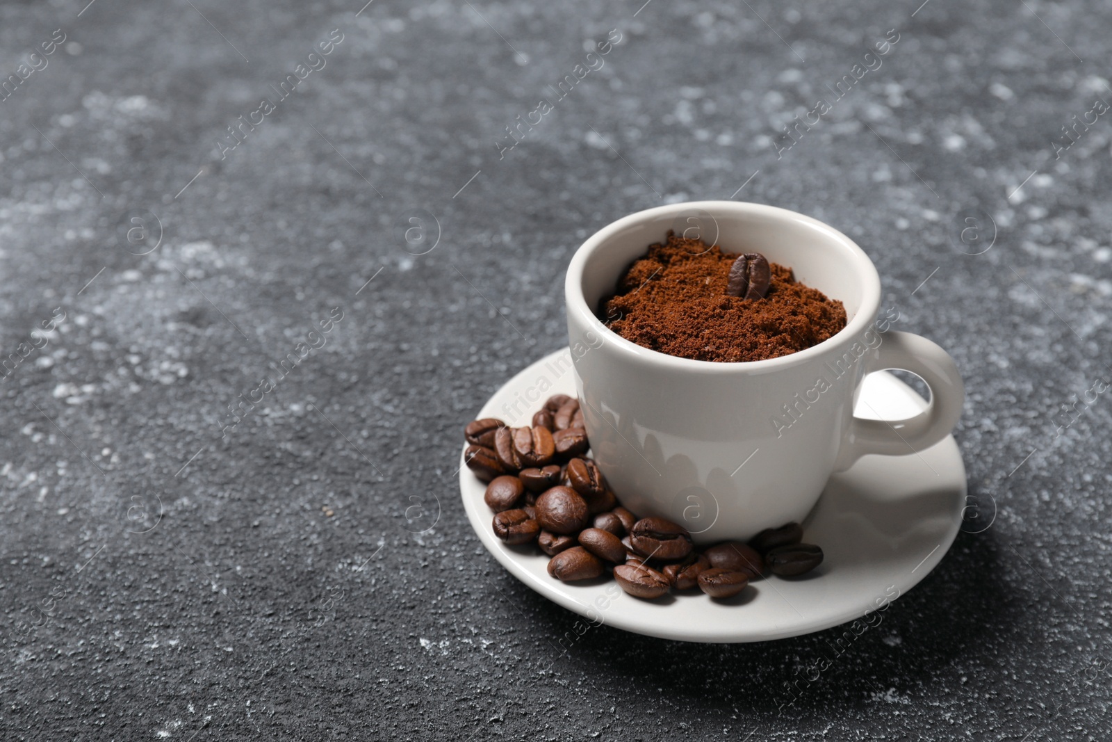 Photo of Cup with roasted beans and ground coffee on dark grey table. Space for text