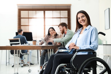 Photo of Young woman in wheelchair with colleagues at office