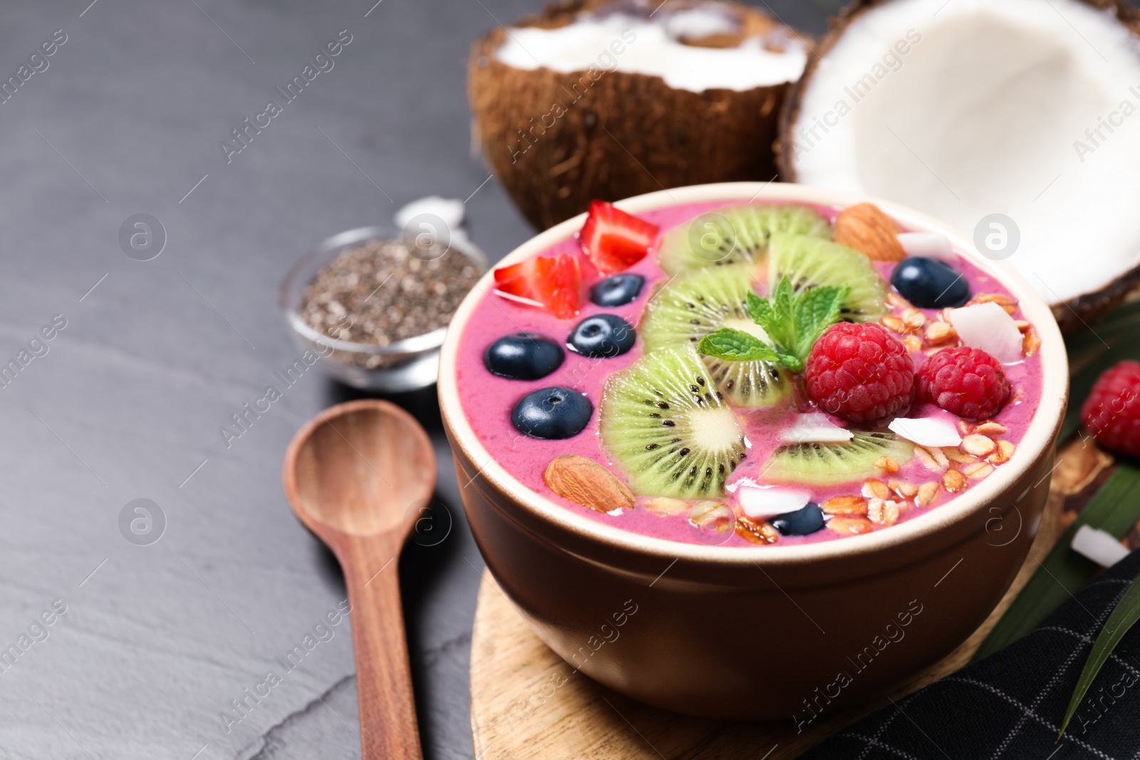 Photo of Delicious acai smoothie with granola and fruits served on black table, closeup. Space for text