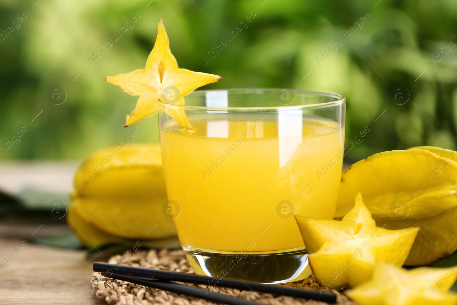 Photo of Delicious carambola juice and fresh fruits on wooden table against blurred background, closeup