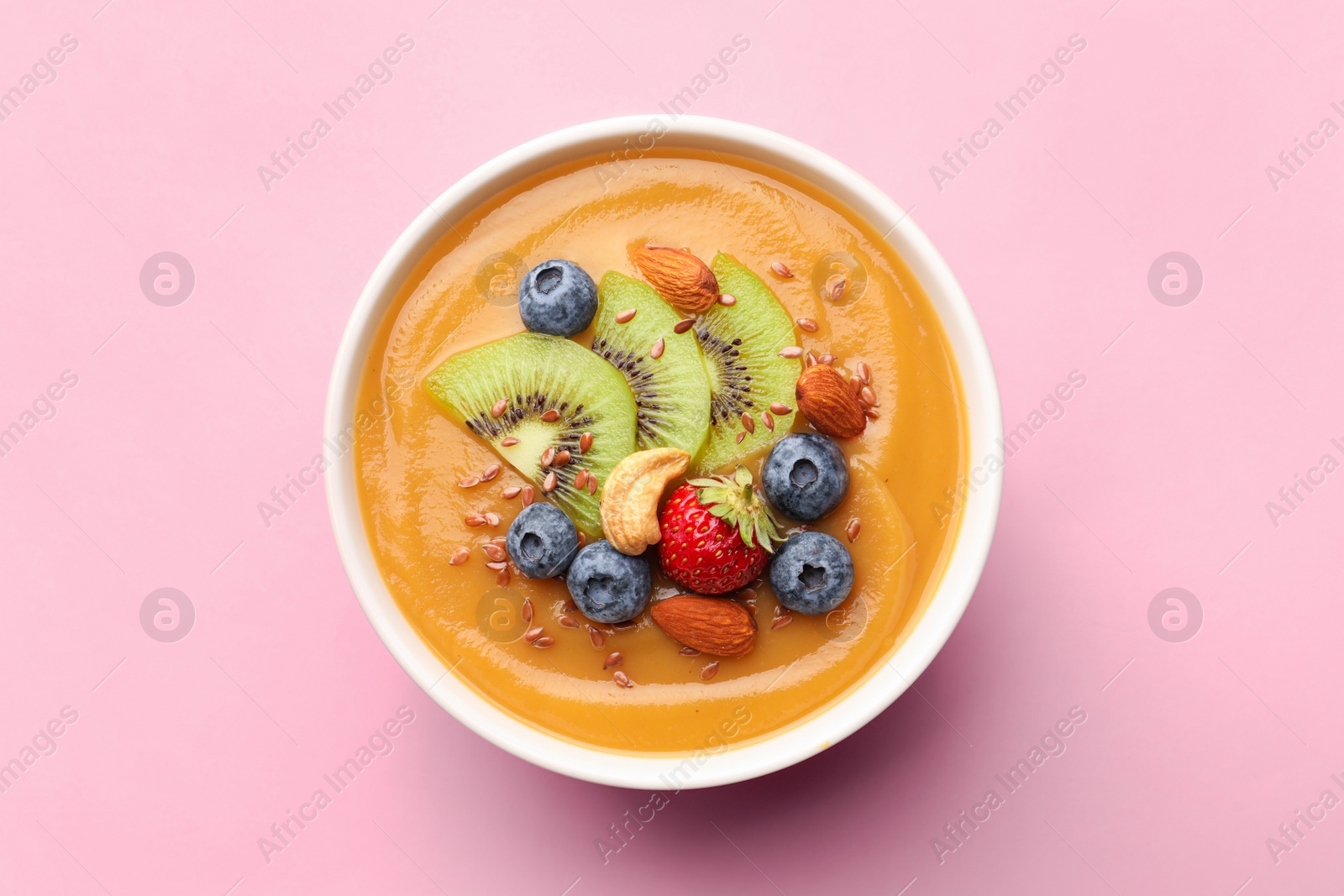 Photo of Delicious smoothie bowl with fresh berries, kiwi and nuts on pale pink background, top view