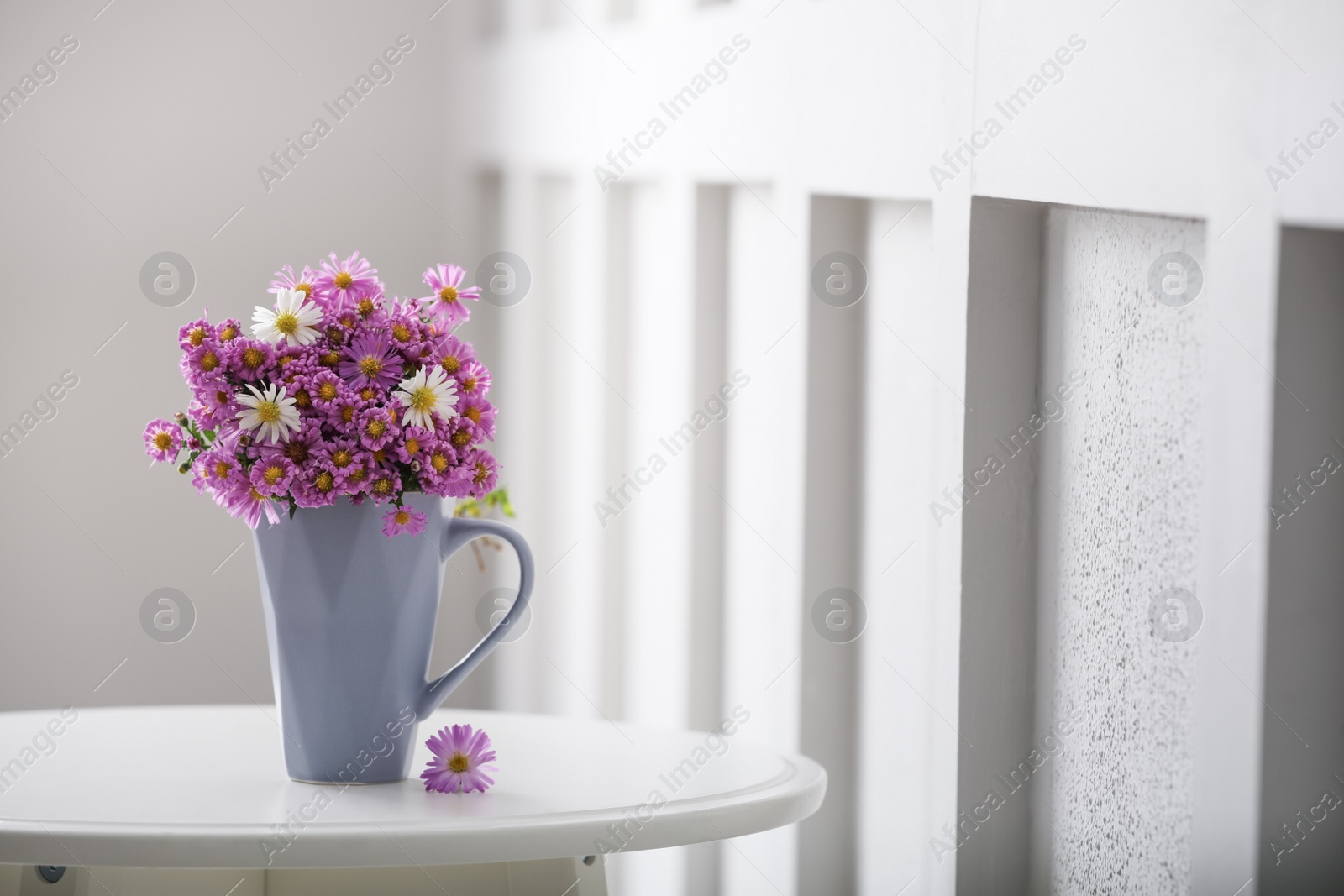 Photo of Cup with beautiful flowers on white table in light room. Space for text