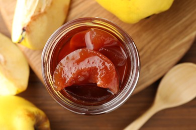 Photo of Tasty homemade quince jam in jar and fruits on wooden table, flat lay