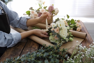 Photo of Florist making beautiful wedding bouquet at wooden table, closeup