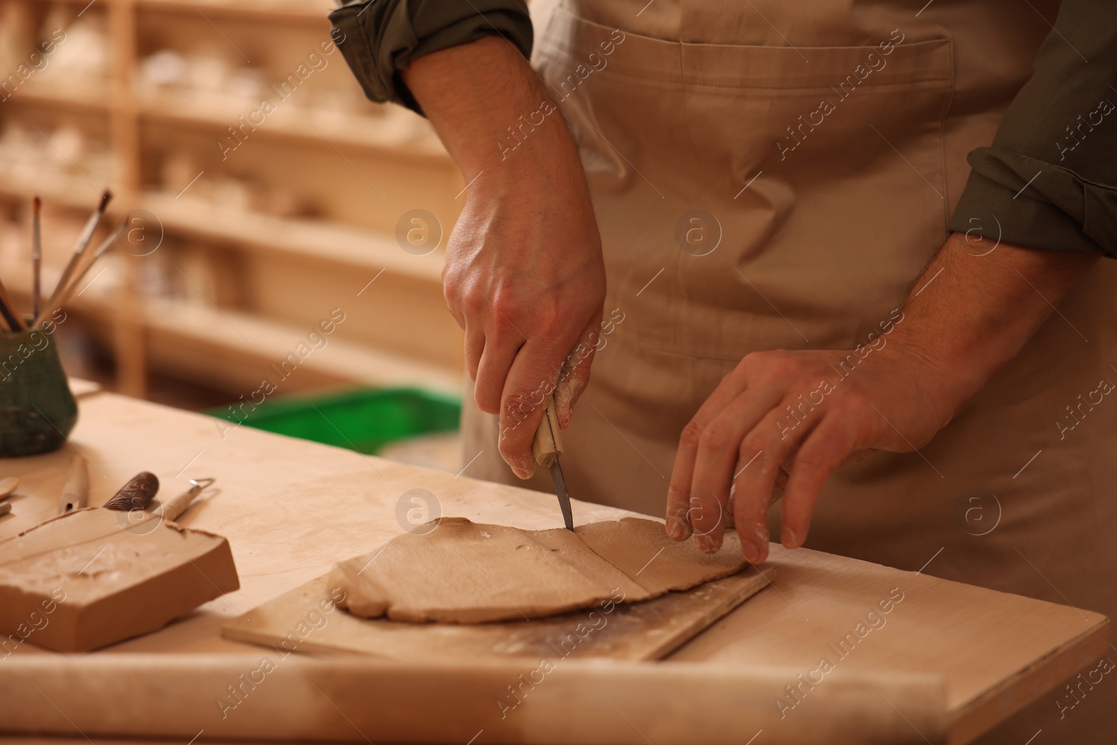 Photo of Man cutting clay with knife at table indoors, closeup