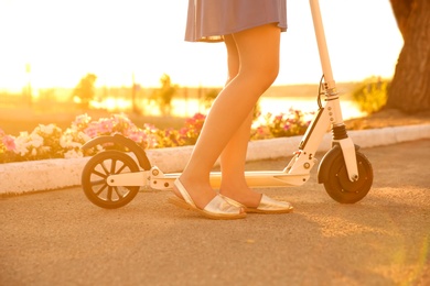 Photo of Woman riding electric kick scooter outdoors on sunny day, closeup