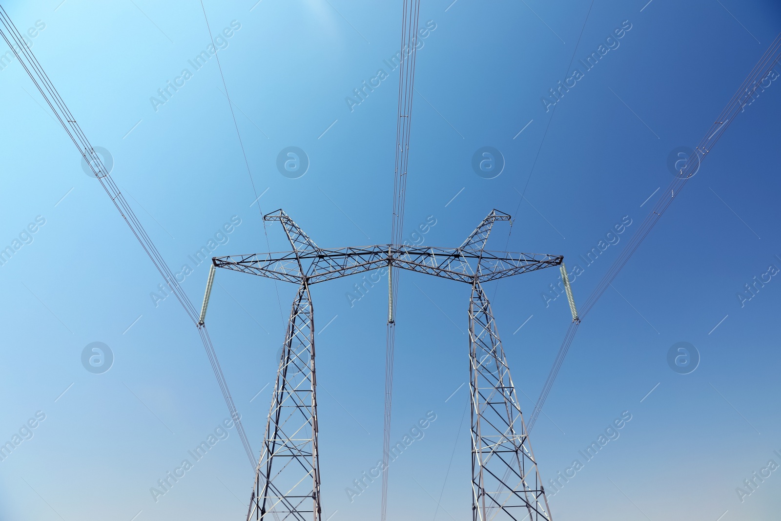 Photo of High voltage tower with electricity transmission power lines against blue sky, low angle view