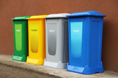 Photo of Many color recycling bins near brown wall outdoors