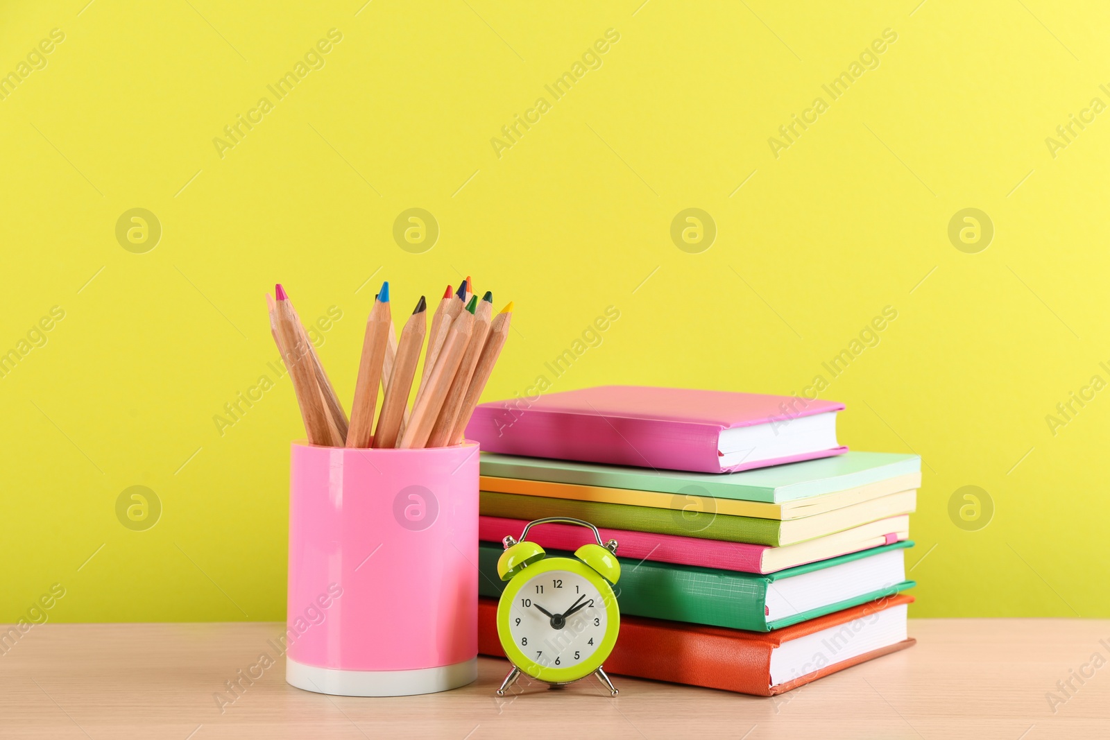 Photo of Set of school stationery and alarm clock on table against yellow background. Back to school