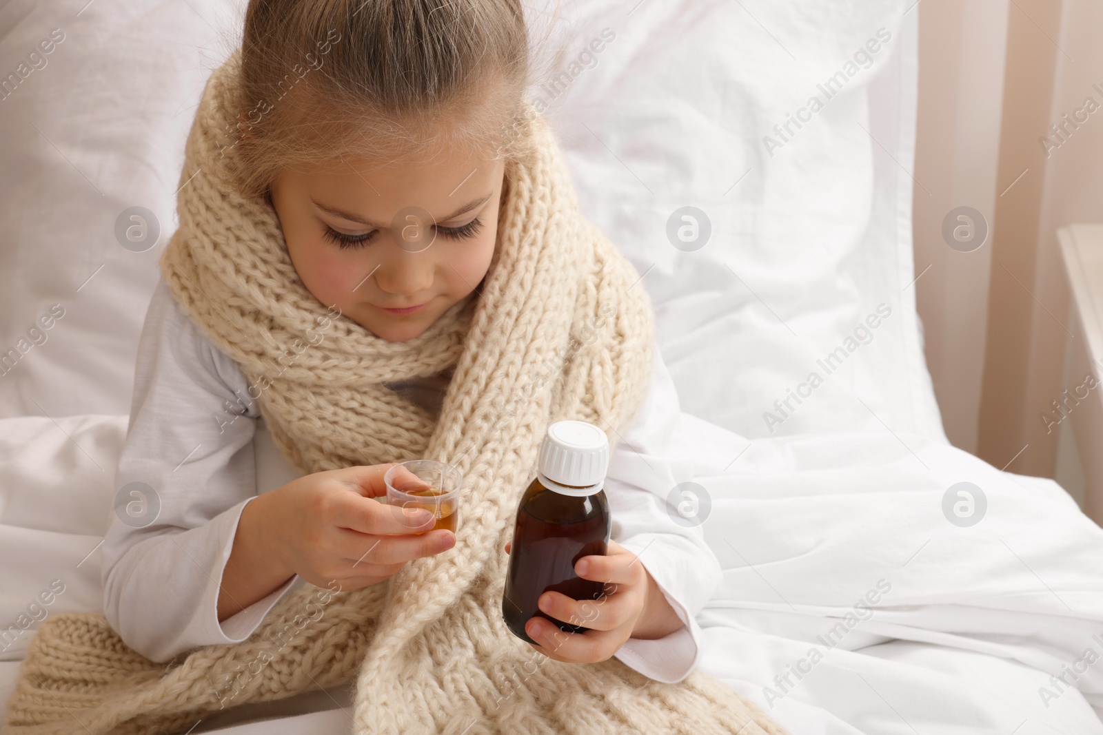 Photo of Sick girl taking cough syrup on bed at home, space for text. Cold medicine