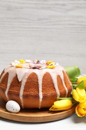 Delicious Easter cake decorated with sprinkles near egg and beautiful tulips on white wooden table. Space for text