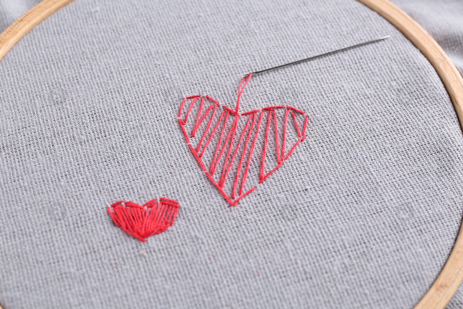 Photo of Embroidered red hearts and needle on light grey cloth, closeup