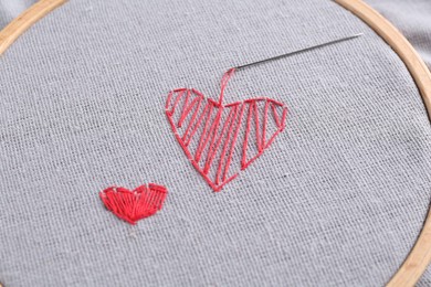 Photo of Embroidered red hearts and needle on light grey cloth, closeup