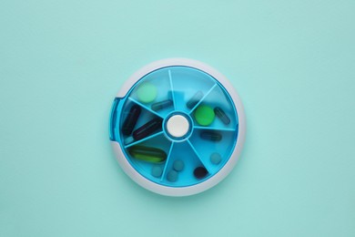 Plastic box with different pills on light blue background, top view