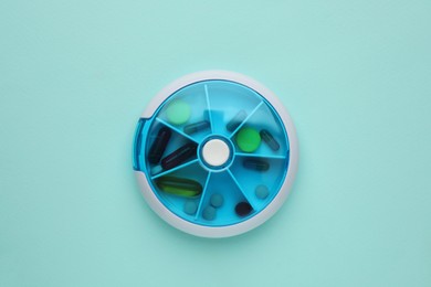 Photo of Plastic box with different pills on light blue background, top view