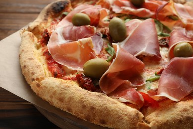 Tasty pizza with cured ham, olives and sun-dried tomato on wooden table, closeup